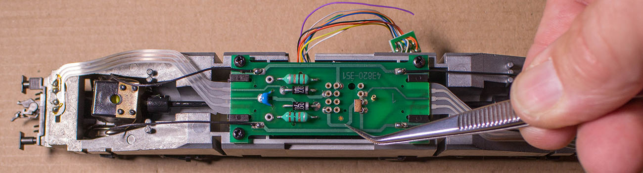 Die Pinzettenspitze zeigt auf die sternförmige Markierung, dies ist der Pin 1, auf diese Seite wird das rote Kabel des Decoders positioniert